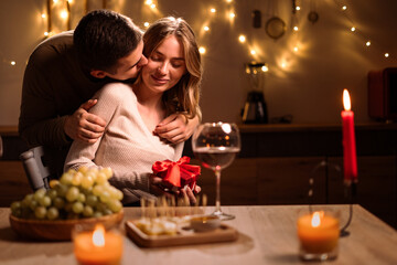 Valentine's Day concept. Celebrating Valentines Day at home. Young couple in love hug while have romantic dinner.