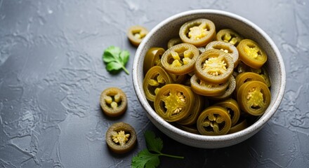 Fototapeta premium A bowl overflowing with sliced pickled jalapeños complemented by scattered leaves on a textured gray surface