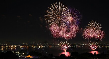 Fireworks burst in the night sky above a citys illuminated waterfront