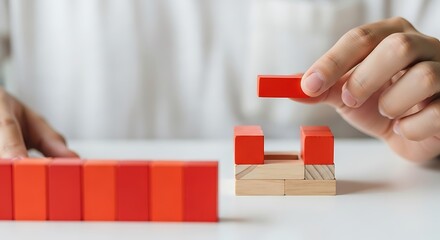 Hand placing red block on wooden structure image