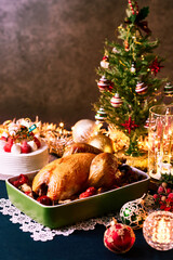 クリスマスツリーとイルミネーションを背景に、ローストチキンとイチゴのクリスマスケーキが並ぶ華やかな食卓　家族や恋人と過ごすホリデーシーズンの特別なディナーシーン