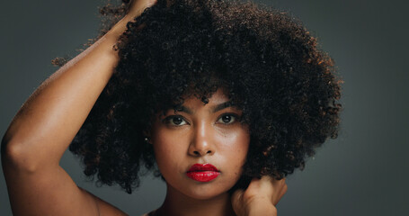 Fototapeta premium Portrait, face and woman in studio with afro, makeup and organic cosmetic for healthy curls. Proud, confident and African female person with beauty, natural hair care and lipstick on gray background