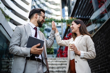 Business people giving high five outdoors while smiling and holding tablet and coffee