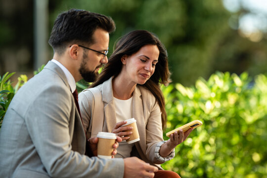Business colleagues enjoying coffee break and using smartphone outdoors
