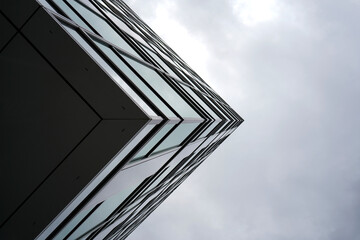 Abstract view of modern glass building corner against cloudy sky, highlighting sharp geometry, minimal lines, and urban architectural elegance