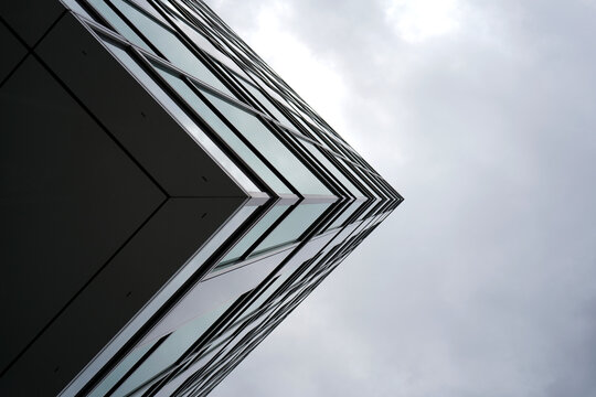 Abstract view of modern glass building corner against cloudy sky, highlighting sharp geometry, minimal lines, and urban architectural elegance