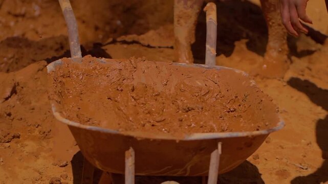 Construction workers mixing mud and clay in a wheelbarrow, employing traditional techniques for adobe brick building in Chapada dos Veadeiros, Brazil