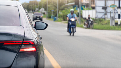 Rear side of grey car turn on brake light. Stop on asphalt road. Opposite of road with motorcycle with driving in city upcountry of Thailand.