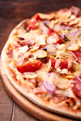 Pizza with salami, tomatoes and mozzarella cheese. Rustic wooden background. Soft focus. Copy space.	