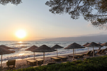 Beautiful sandy beach with parasols and sun loungers on the Turkish Aegean coast near Izmir and the Greek islands in the Mediterranean Sea in the evening sun in summer, Turkey Europe and Asia