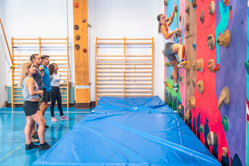 Determined sportswoman climbing wall with friends watching in gym