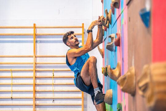 Determined male athlete climbing challenging indoor wall in gym
