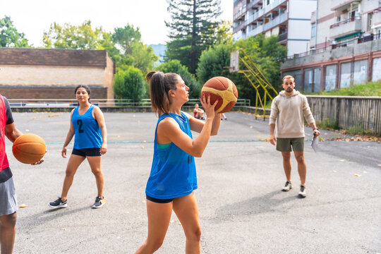 Female basketball player shooting ball during training outdoors with coach and teammates - Powered by Adobe