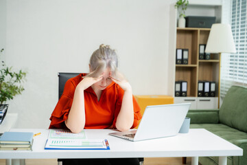 Overwhelmed young woman stressed at her desk with a laptop and reports in a modern office. Concept...