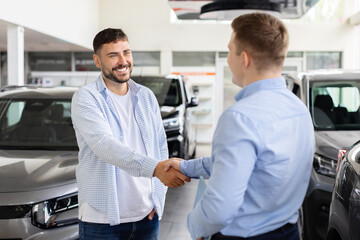 Fototapeta premium Smiling man shaking hands with car dealer at dealership, customer finalizing automobile purchase near vehicles. Lifestyle, agreement, transport and consumer trust