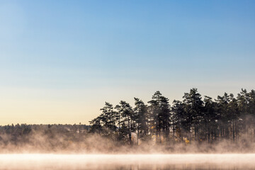 Fototapeta premium Morning mists by a lake in the forest in autumn