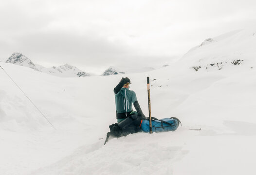 A ski guide holds his hat at a helicopter landing in a snowfield.