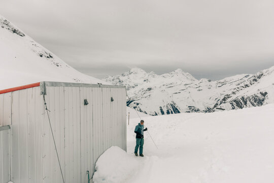 A man stands next to a backcountry hut in the mountains.