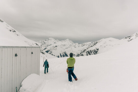 Two men stand outside a backcountry hut in the mountains in winter.