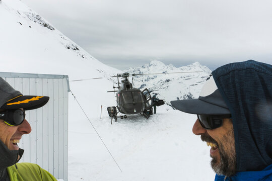 Two men laugh as a helicopter lands at a backcountry hut.