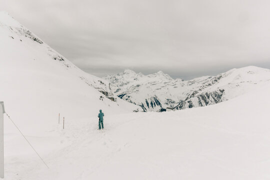 A man stands alone in the mountains near a backcountry hut.