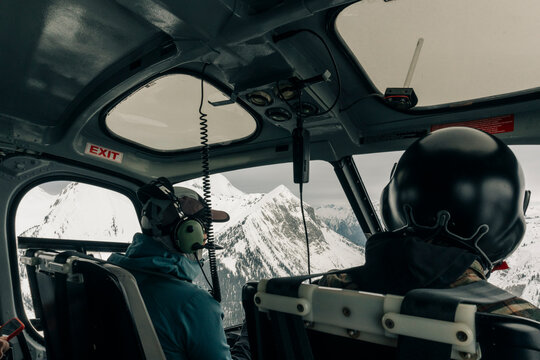 Two people in the front of a helicopter in the mountains in winter.