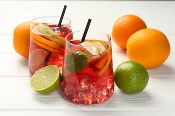 Tasty punch with ice, mint and slices of fruits in glasses on white wooden table, closeup. Refreshing drink