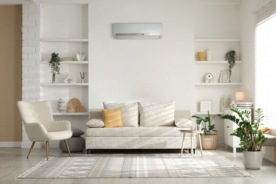 Contemporary furniture, houseplants and decor in living room. Air conditioner keeping comfortable temperature indoors