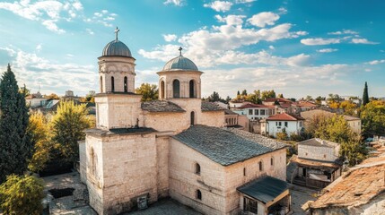 Fototapeta premium Old stone church with domes surrounded by houses and trees under blue sky in historic european town