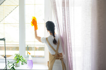 Woman in rubber gloves and apron manually washes window balcony of house with rag cleaner and mop inside interior. Restoring order and cleanliness in spring, cleaning servise