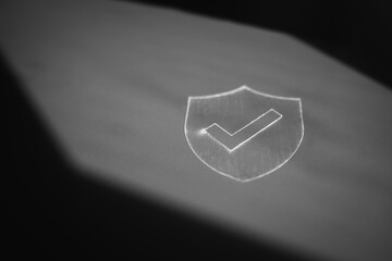 Black and white close-up of a shield icon with checkmark symbol, representing digital security, data protection, privacy assurance, and verified access on dark background.