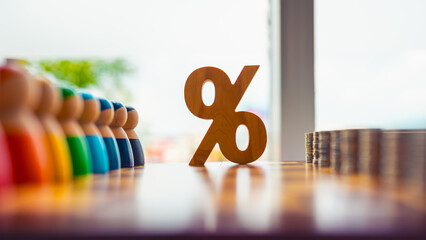 Colorful wooden figures, percentage symbol, and stacked coins on table, symbolizing interest rates,...