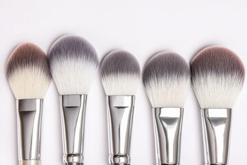 A set of five makeup brushes with varying brush head shapes and colors, arranged neatly on a light background.