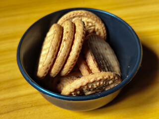 Stack of round wheat crackers in a small black bowl, placed on a wooden table.