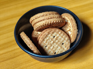 Stack of round wheat crackers in a small black bowl, placed on a wooden table.