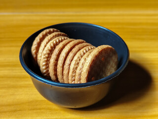 Stack of round wheat crackers in a small black bowl, placed on a wooden table.