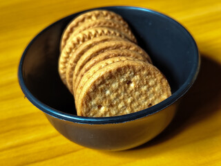 Stack of round wheat crackers in a small black bowl, placed on a wooden table.