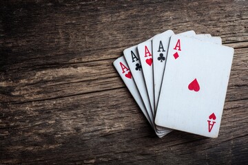 Five playing cards all Aces arranged on a dark wooden surface