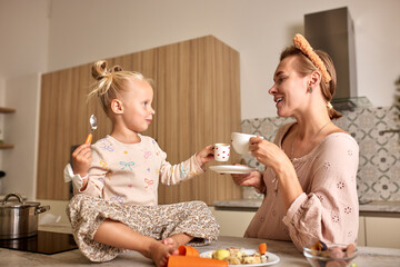 Mother and daughter having a joyful tea time together in the kitchen