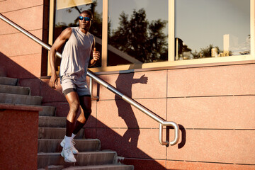Man running down stairs outdoors in athletic gear and sunglasses