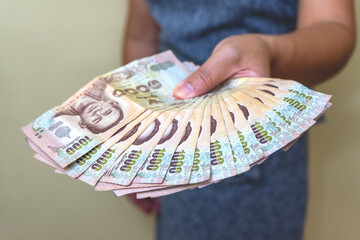 The hand of a successful Asian woman holds Thai money, a visual of her hard work paying off and her financial success.