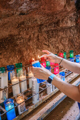 Visitor lighting colorful votive candles in the sacred Holy Cave of Montserrat near Barcelona, Spain. This mystical grotto attracts thousands of pilgrims