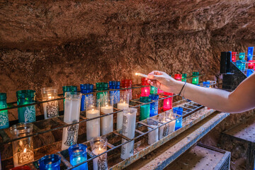 Person Lighting Colorful Votive Candles In Holy Cave Of Montserrat Monastery Barcelona Spain. Religious Pilgrimage Site, Prayer Candles, Sacred Grotto