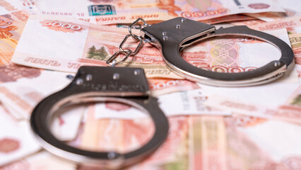 A pair of handcuffs are on top of a pile of money. The handcuffs are silver and appear to be brand...