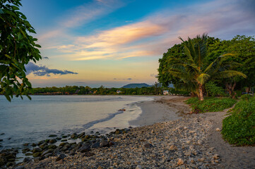 Rocky and sandy shoreline of Tamarin Public Beach in Mauritius with palm trees and calm waters at sunset.