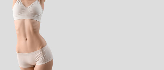 Slim young woman in underwear on light background