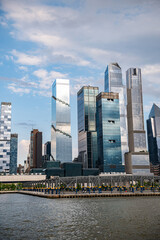 Fototapeta premium Manhattan skyline by the river. Skyscrapers tower over the river in Manhattan, highlighting NYC's vibrant architecture on a sunny day.