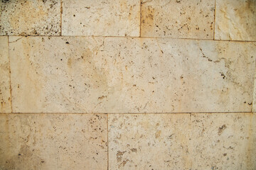 Textured wall of smooth rectangular stone blocks in light beige shades.