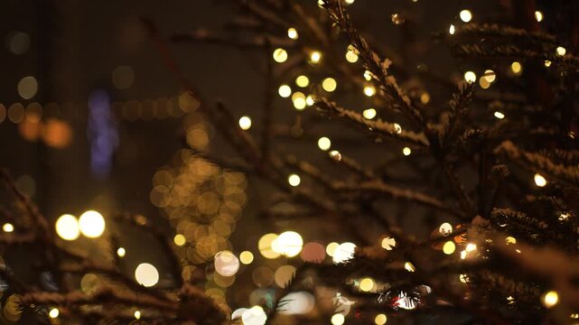 Festive christmas tree branches covered in snow, adorned with twinkling fairy lights, create a magical atmosphere against a backdrop of blurred city lights at night
