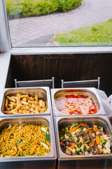 Buffet with Thai food including noodles, spring rolls, curry, and stir-fried vegetables in stainless steel trays.